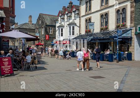 People tourists visitors walking in the town centre shops outdoor outside cafe in summer Main Street Keswick Cumbria England UK Britain Stock Photo