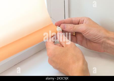 Close-up male hands are attaching the details to the roller blinds on the window. Roller shutter installation. Stock Photo