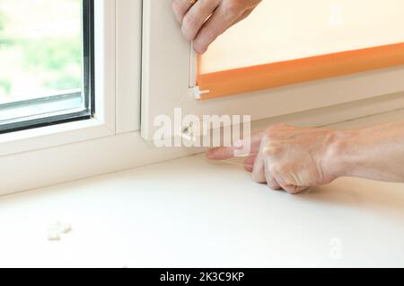 Installation of roller blinds. Male hands close-up install blinds on the window. Stock Photo