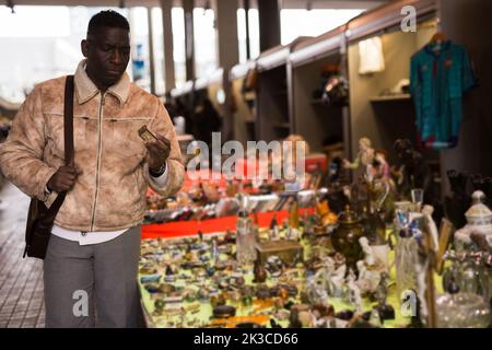 ordinary Afro-American guy considers things sacond hands on flea market Stock Photo