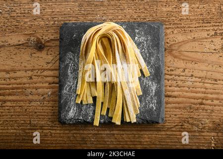 Top view of freshly prepared raw homemade Italian tagliatelle pasta with flour placed on slate board on wooden table in kitchen Stock Photo