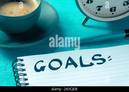 Goal setting. A notepad with the handwritten word on a desk, with a pen, an alarm clock, and a cup of coffee. The concept of resolutions, writing a plan Stock Photo