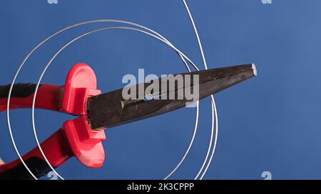 Cutting and holding pliers with coil of wire, blue background Stock Photo