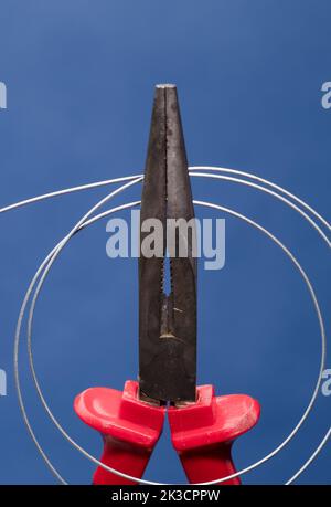 Cutting and holding pliers with coil of wire, blue background Stock Photo