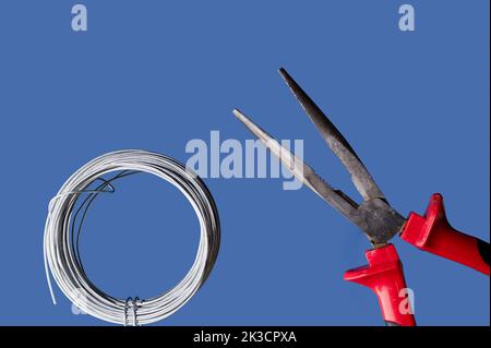 Cutting and holding pliers with coil of wire, blue background Stock Photo
