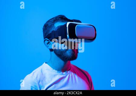 Casual bearded man trying VR headset and exploring another world in neon lights. Stock Photo