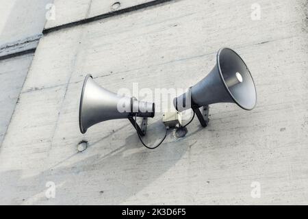 Pair of big retro loudspeakers mounted on grey concrete cement wall. Air raid nuclear strike alert speaker siren. Urgent or emergency announcement Stock Photo