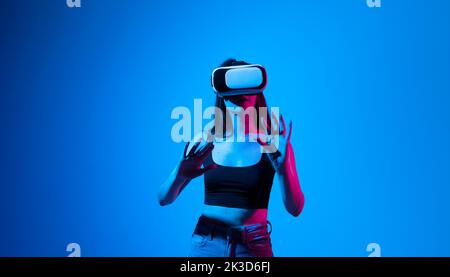 Impressed brunette woman using virtual reality headset, getting immersed experience, interacting with immersive digital world, testing VR technology. Stock Photo