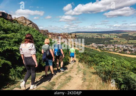 Group of people walking down a path towards the Cow and Calf Rocks on Ilkley Moor on a summer's day, West Yorkshire, England, UK Stock Photo