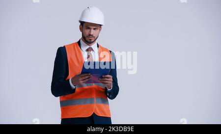serious contractor in hardhat holding clipboard and looking away isolated on grey,stock image Stock Photo