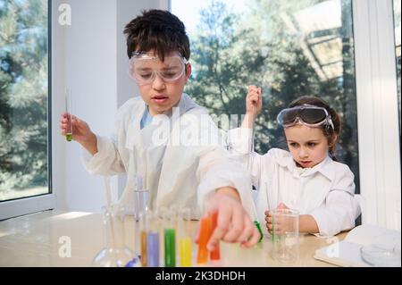 Cute smart kids learning Chemistry in chemical lab. Little children at lesson. Elementary age students doing experiments Stock Photo