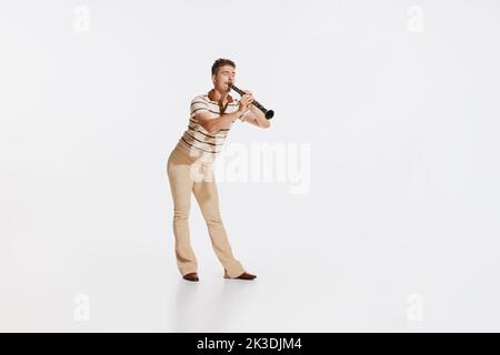 Young man wearing 50s, 60s fashion style clothes playing clarinet on white studio backround. Music, art, inspiration concept Stock Photo
