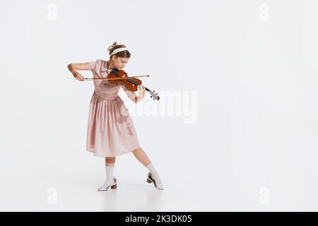 Charming beautiful young girl playing violin isolated over white studio background. Tender, lovely sound. Concept of retro, vintage style Stock Photo