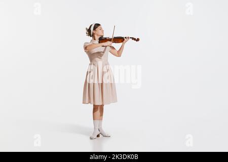 Charming beautiful young girl playing violin isolated over white studio background. Tender, lovely sound. Concept of retro, vintage style Stock Photo