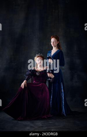 Portrait of two beautiful women in image of royal persons, queen and princess, isolated over dark background Stock Photo