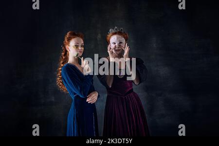 Portrait of two beautiful women in image of queens in face masks over dark background. Skincare Stock Photo