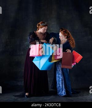 Portrait of two beautiful women in image of queens isolated over dark background. Great sales Stock Photo