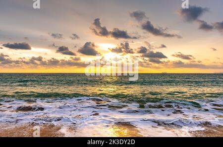 Beautiful sunset above sea or ocean. Vibrant and soft colors, magic light. Small clouds on the sky, reflection of sun in the water and sand on beach. Stock Photo