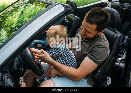 Dad shows his little son how to drive car while sitting behind wheel Stock Photo