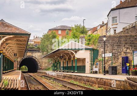 Two railway station canopies supported by green columns are aside the entrance to a tunnel. Rails lead into the tunnel and the a sky with cloud is abo Stock Photo