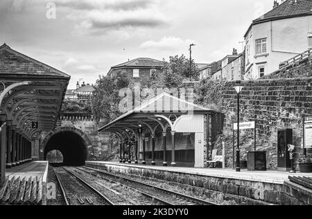 Two railway station canopies supported by green columns are aside the entrance to a tunnel. Rails lead into the tunnel and the a sky with cloud is abo Stock Photo