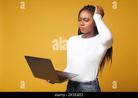 Female student pondering and looking at the laptop screen while writing lecture in a notebook. Young woman using laptop computer, solving tasks Stock Photo