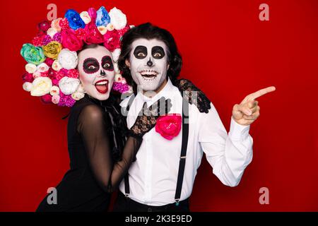 Photo of spooky two people man lady cuddle direct finger empty space amazed festival beginning promo wear black dress death costume roses headband Stock Photo
