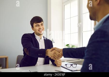 Two smiling business people shaking hands after signing the contract sitting in office. Stock Photo