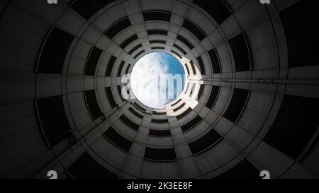 Spiral entrance tube of a parking garage made of concrete with view of blue sky and white clouds. Wide angle shot from bottom to top. Stock Photo
