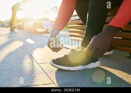 Close-up of hands of young sportsman tying shoelace of black sport shoe while sitting on bench in urban environment in the morning Stock Photo