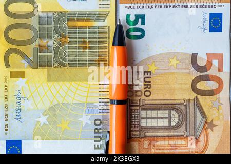 financial settlements in the euro zone, concept, 50 and 200 euro banknotes stacked next to each other, between them an orange pen, taxes in the europe Stock Photo