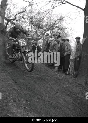1954, historical, outside on steep rough terrain in a forest, spectators watching a competitor riding a motorcycle of the era, in a scramble or trial race at Seacroft, Leeds, England, UK, organised by the West Leeds Motor Club. Stock Photo