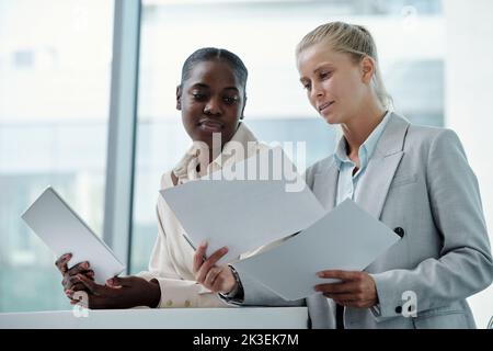 Two young successful businesswomen looking through financial documents, analyzing data and discussing it at meeting Stock Photo