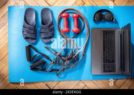 Pool slippers and a laptop. Fitness items and laptop. Rubber expanders and red dumbbells. Dumbbells and laptop. View from above. Stock Photo