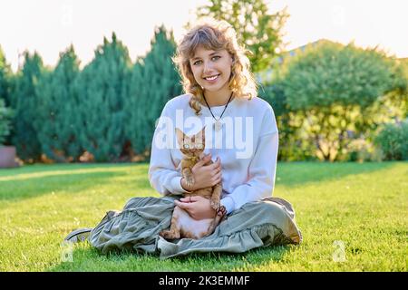 Outdoor portrait of teenage girl with pet cat in her arms sitting on grass Stock Photo