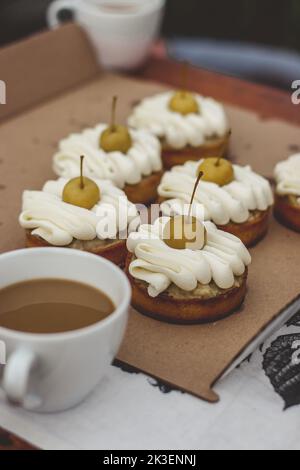 Delicious cake cupcakes with a chocolate base and white whipped cream on it and a yellow cherry. A white coffee mug is next to it. Stock Photo