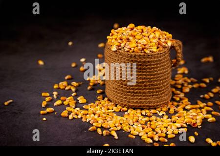 Grains of corn in jute sack and scattered grains around on a dark background Stock Photo