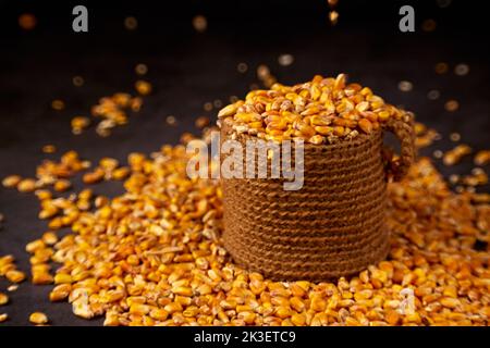 Corn grains in a jute bag and scattered grains around on a dark background Stock Photo