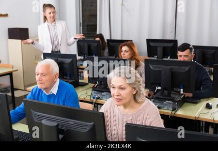 Young and mature colleagues sitting and working on computers Stock Photo