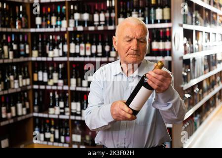 Elderly man chooses red wine in a liquor store Stock Photo