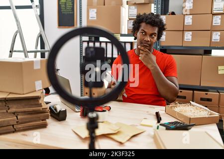 African man working at small business ecommerce doing video tutorial serious face thinking about question with hand on chin, thoughtful about confusin Stock Photo