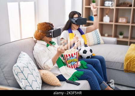 Two women mother and daughter watching soccer match using vr glasses at home Stock Photo