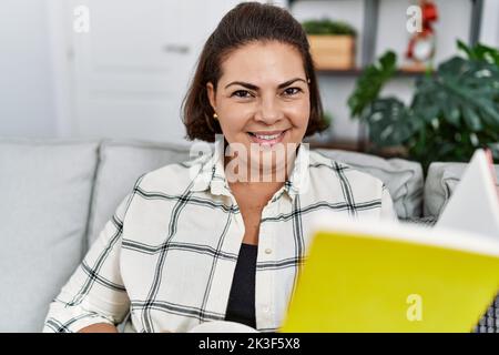 Middle age hispanic woman smiling confident reading book at home Stock Photo