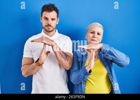 Young brazilian mother and son standing over blue background doing time out gesture with hands, frustrated and serious face Stock Photo