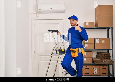 Young hispanic man working at renovation smiling happy and positive, thumb up doing excellent and approval sign Stock Photo