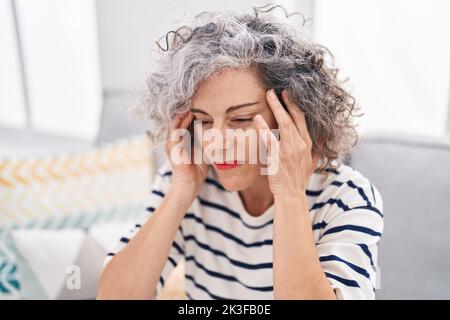 Middle age grey-haired woman suffering for headache sitting on sofa at home Stock Photo