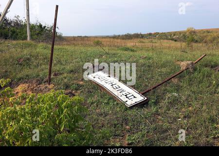 KHARKIV REGION, UKRAINE - SEPTEMBER 26, 2022 - A sign with the name of the village of Dementiyivka, recently liberated from russian invaders, fallen to the ground, Kharkiv Region, north-eastern Ukraine. Stock Photo