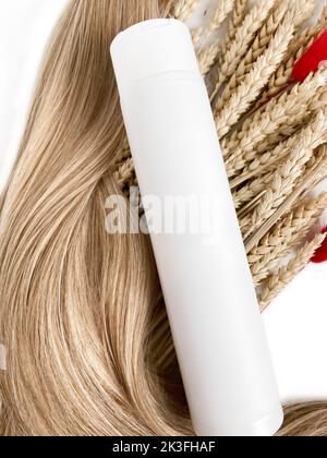 A strand of blond hair with a bottle of shampoo on a white background. Close-up. Stock Photo