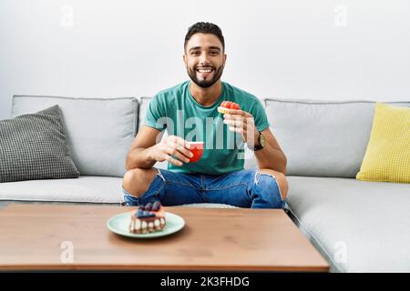 Young arab man having breakfast sitting on sofa at home Stock Photo