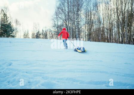 mom and little son in a blue jacket in a snowy forest ride in a tubing on a cold day. Stock Photo
